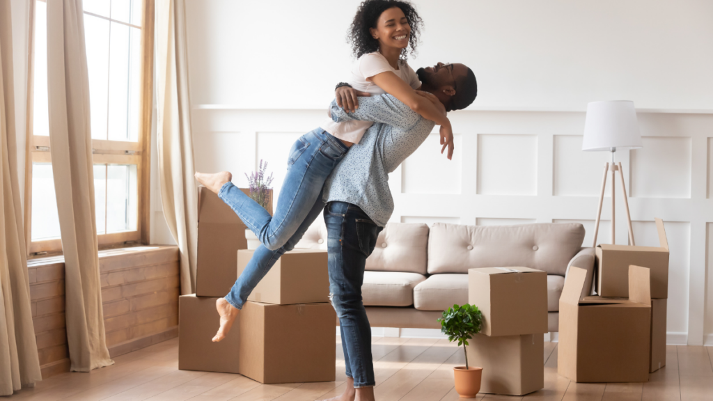 Image shows a happy couple in a home with boxes showing closing day.