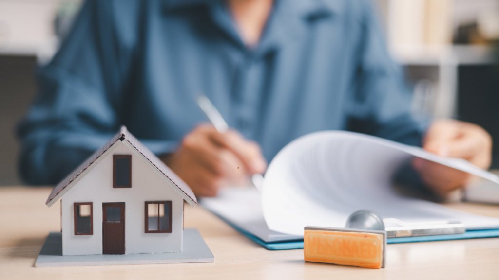 Image shows a person signing paperwork buying a home