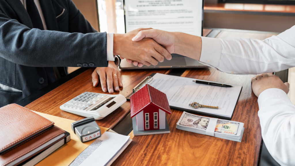 Image shows two people shaking hands beacause the buyer's offer has been accepted. There's a calculator, mini house, key and paperwork showing. 